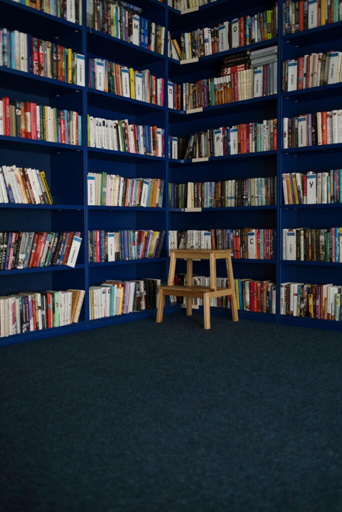 A tranquil library corner featuring blue bookshelves filled with various books and a small wooden stool.